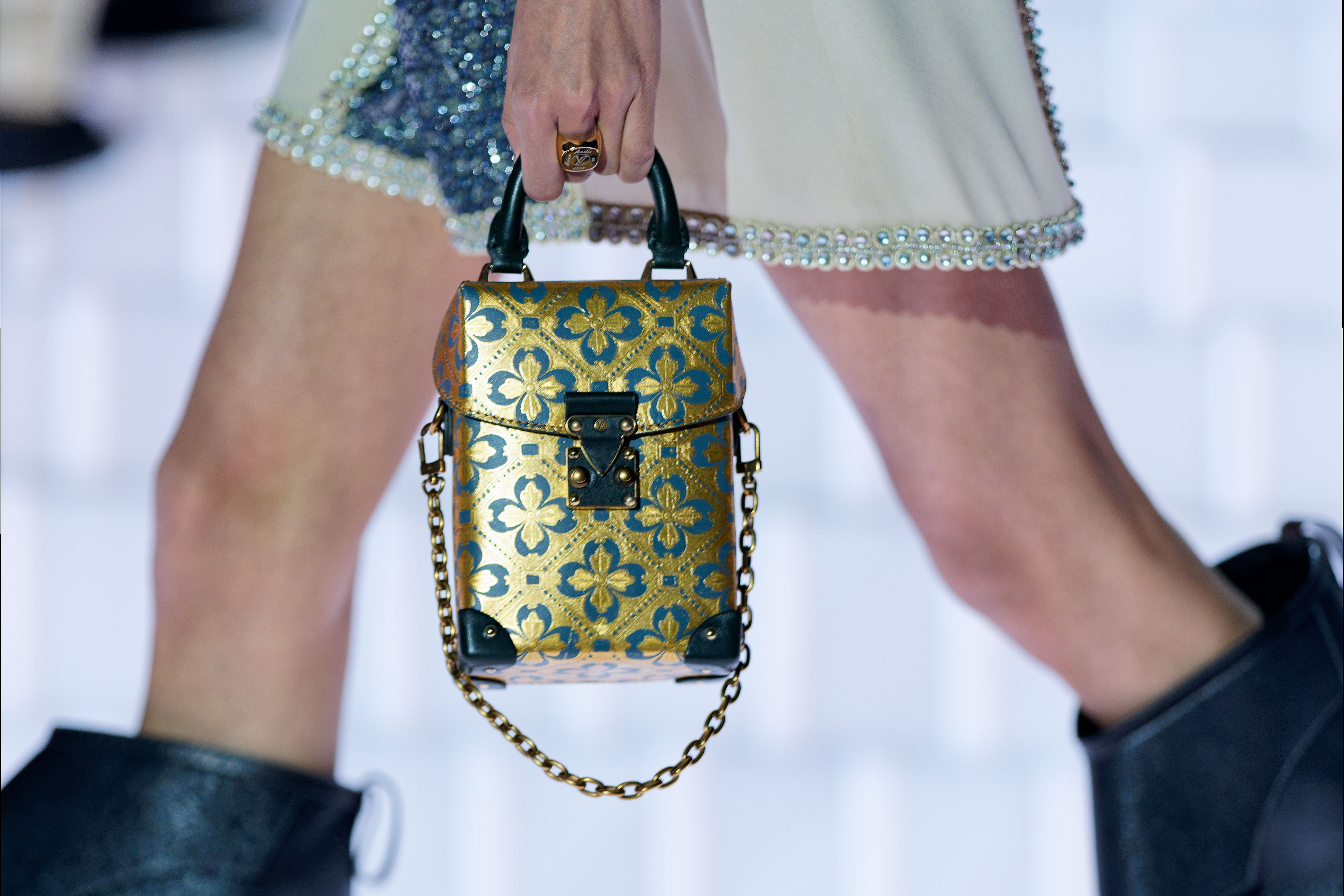 Model holding a gold and blue Louis Vuitton handbag.