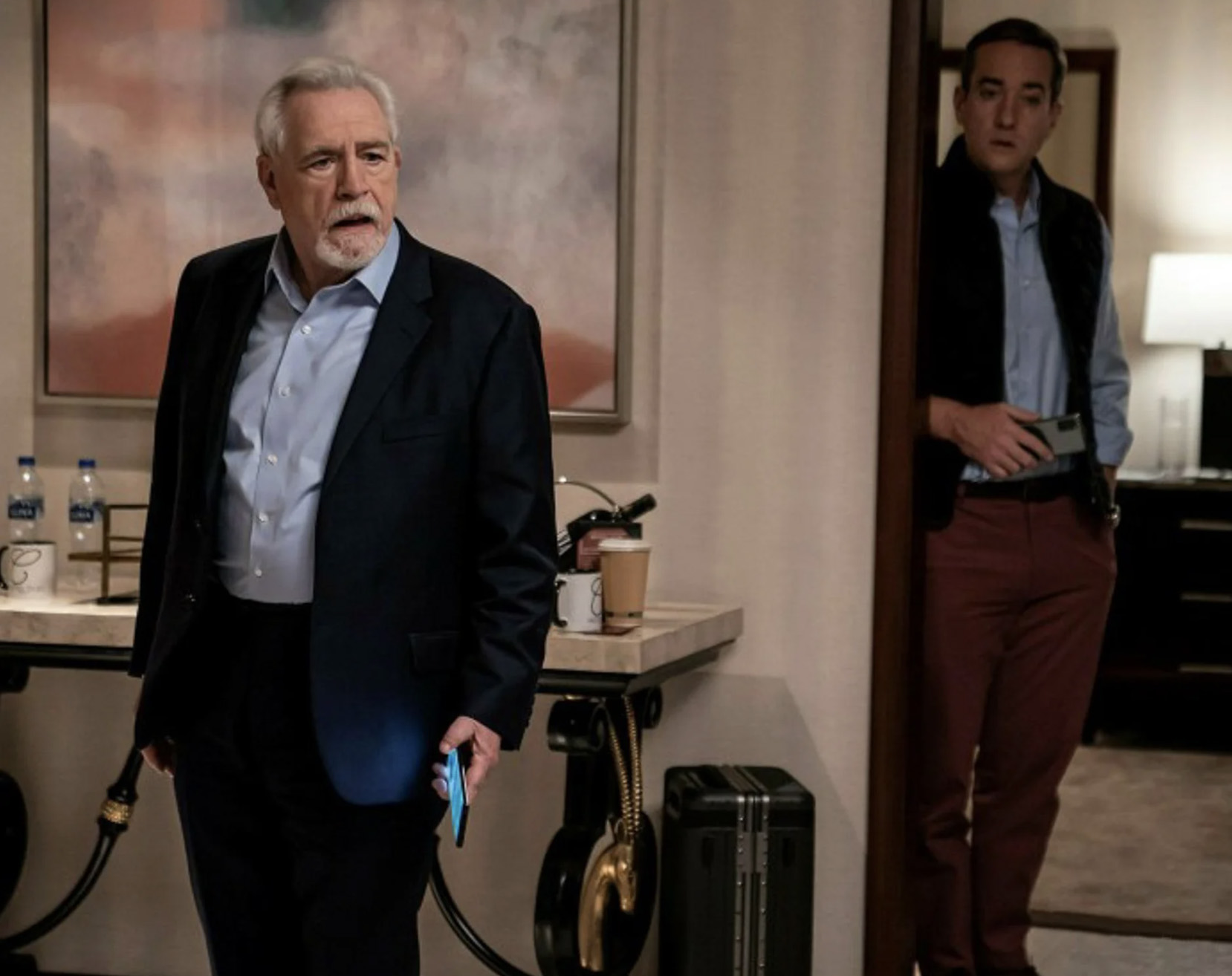Two men in suits in a hotel hallway.