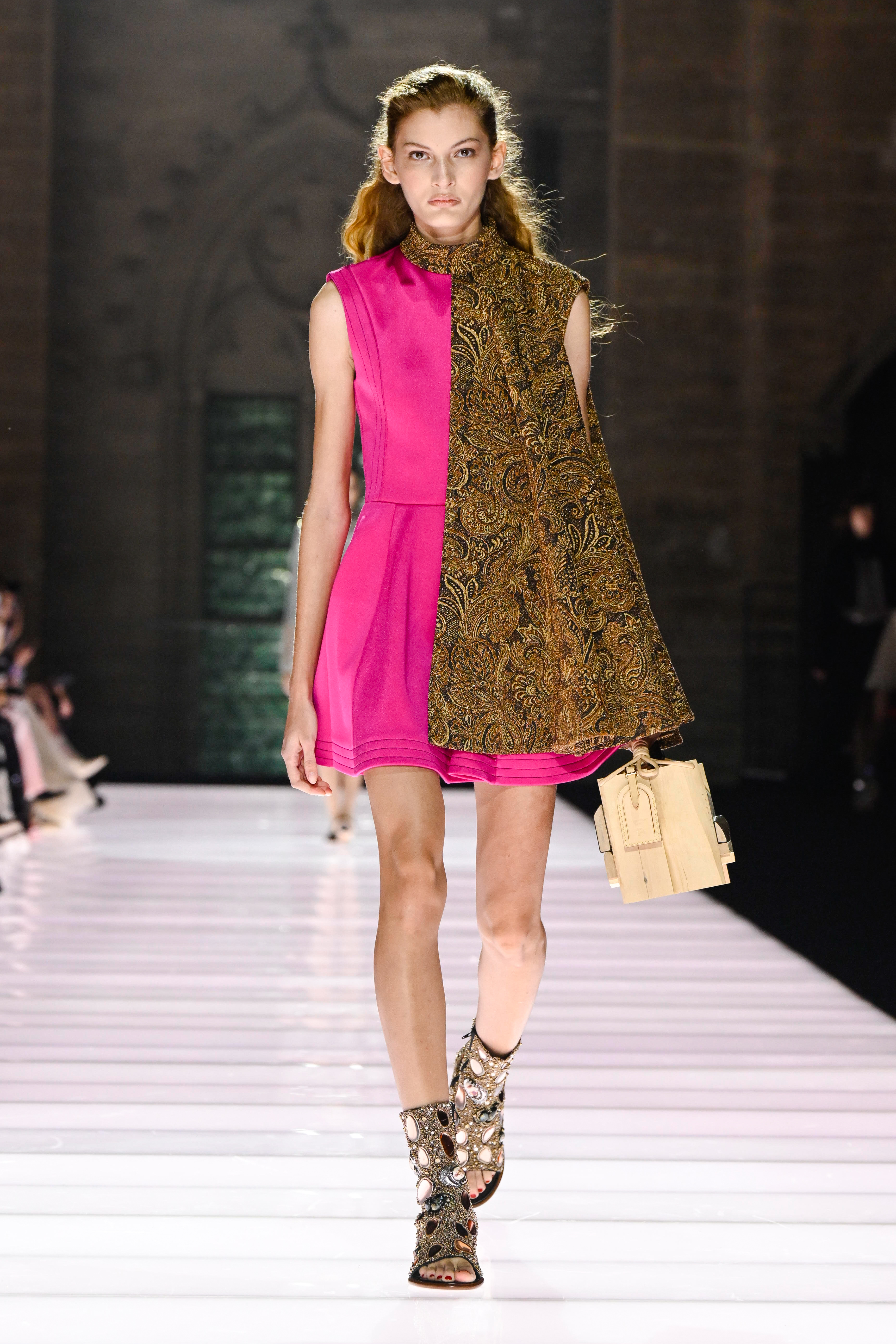 Model walking a runway in a pink and gold Louis Vuitton dress.